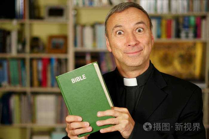 一个看起来严肃和疯狂的天主教神父正在学习, 读圣经, 进入他的图书馆