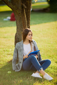 美丽的女孩与她的书在公园背景, 日落
