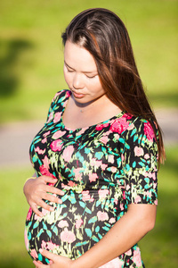 孕妇在花衬衫看了看怀孕胃与夏天背景