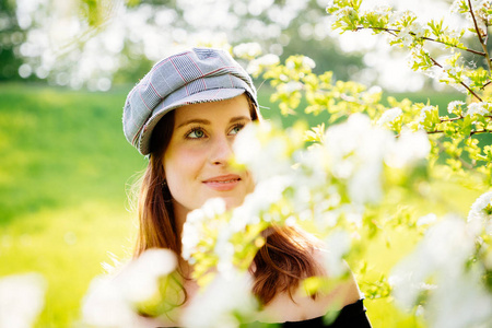 戴着帽子的年轻女子看着树上的白色花朵朦胧