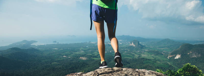 成功女子徒步登山者站在山顶悬崖边上