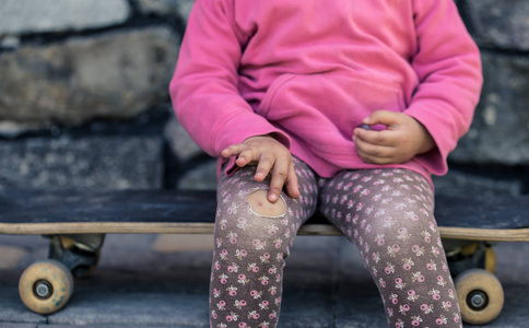 一个漂亮的小女孩摔在滑板上, 膝盖受伤了.照片