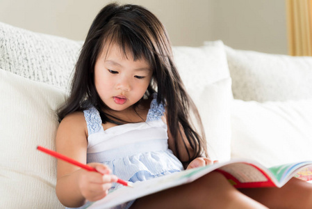 快乐可爱的小女孩微笑着拿着红色的铅笔和图画, 写在一本书上做作业。儿童教育理念