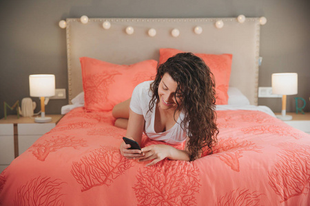 快乐迷人的年轻女子躺在床上阅读短信在她漂亮的卧室