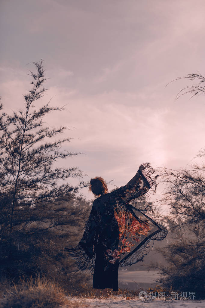 美丽的时尚女人剪影穿着斗篷在日落