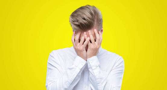 年轻英俊的金发男人带着悲伤的表情捂着脸用手哭着.抑郁症概念照片