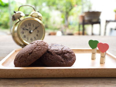 自制软黑巧克力布朗尼饼干放在木盘子上, 在木桌上的心形回形针。饼干背后有黄金复古闹钟