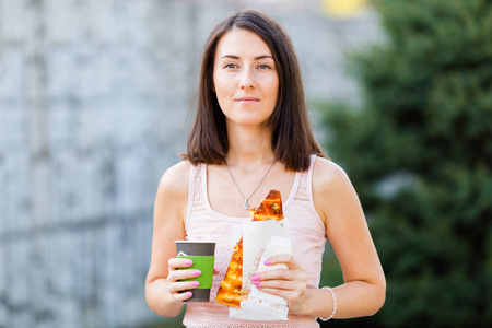 一个年轻女子在吃比萨饼, 手里拿着咖啡的画像。产品演示徽标和文本的样机。生活方式