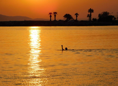 男子游泳在金色的日落, 附近的 Glyfada, 希腊的岸边
