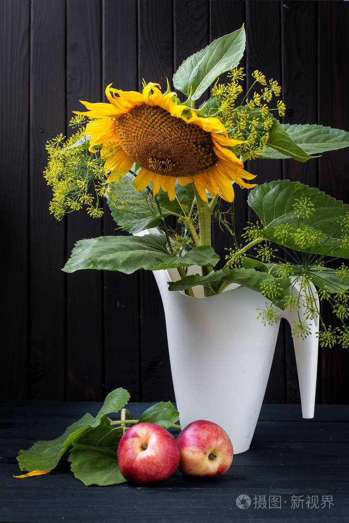 向日葵花在一个浇水罐和两个蜜桃在一个黑暗的木质背景静物