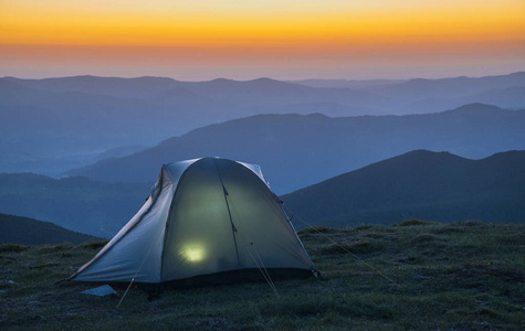 点燃的帐篷反对日出场面在山图片