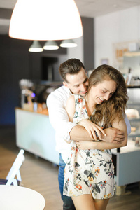 年轻的微笑男人拥抱女孩, 站在咖啡馆附近的桌子