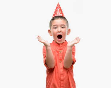 黑发小孩戴着生日帽非常高兴和兴奋, 优胜者表达庆祝胜利尖叫与大微笑和举手