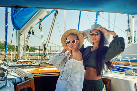 两个年轻漂亮的女人在一个晴朗的日子在游艇上休息。美丽的女人穿着时髦的夏季服装在游艇上