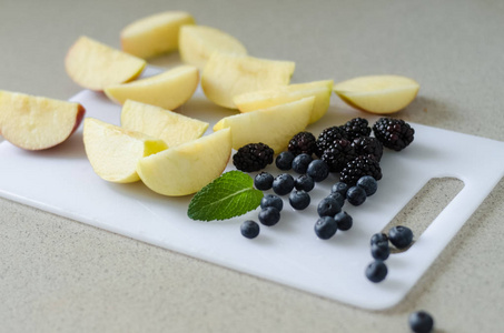 切片新鲜的苹果, 蓝莓, 黑莓和薄荷叶周围, 新鲜的夏季水果从市场上的白色切割板