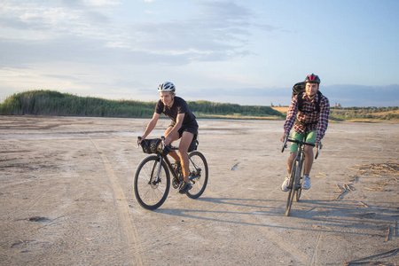 两名年轻男子在一辆带背包和头盔的旅游自行车上骑自行车旅行在乡间小路上骑车。