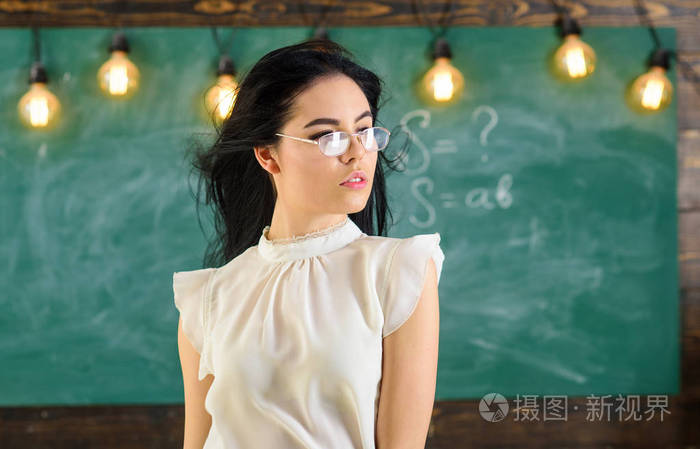 长头发的妇女在白色衬衣站立在教室.夫人在轻松的脸上的严格的老师站