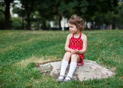 可爱的小孩女孩坐在一个公园里的石头上