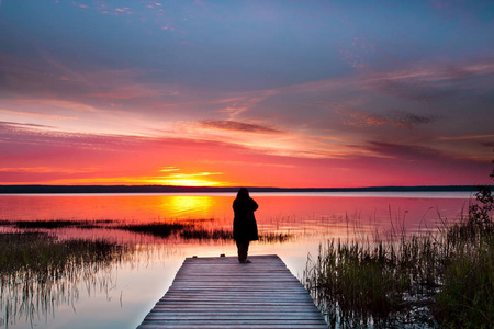 黎明在一个安静的湖。日出, 一个男人的剪影站在木制的码头, 粉红色的色调