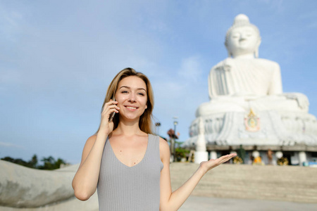 在普吉岛的佛白雕像附近的智能手机聊天的年轻漂亮女孩