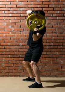 男子 krutin 大厚煎饼从一个哑铃在他的头上, 从事健身, 在橙色砖墙的背景下