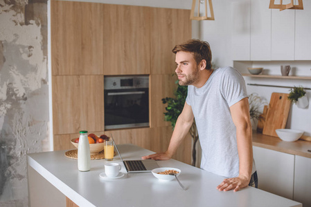 快乐的年轻人站在餐桌上, 早餐和笔记本电脑在厨房