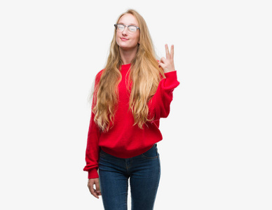 金发女郎身穿红色毛衣显示和指向两个手指, 同时微笑着自信和快乐