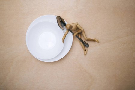 木制的人体模特在白色盘子旁边用金属勺子。营养理念