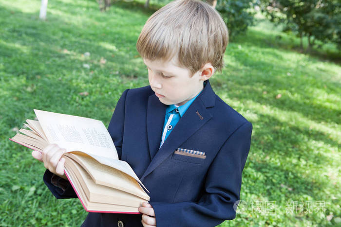 手里拿着书的男孩.这个男孩正在露天看书.男孩拿着一本书.照片-正版商