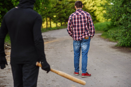 一个穿着黑色衣服的罪犯手里拿着棒球棍攻击一个人.