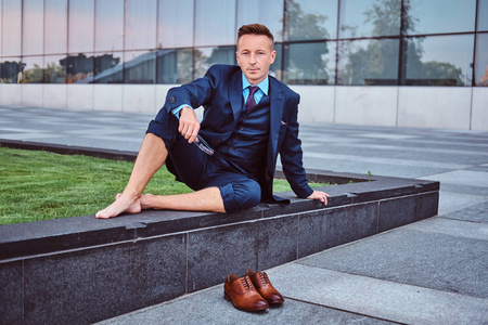 穿着高雅西装的自信商人戴着眼镜, 赤脚坐在城市景观背景上.照片