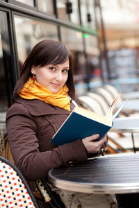 美丽的年轻女孩读一书在巴黎街头咖啡馆