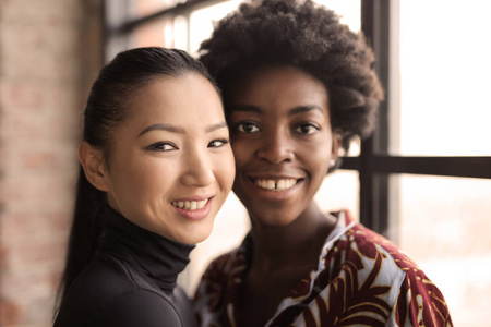 两个女性朋友, 一个非洲女人和一个亚洲女人一起微笑着走进相机