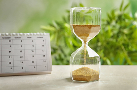 沙漏和日历上表反对模糊的背景。时间管理