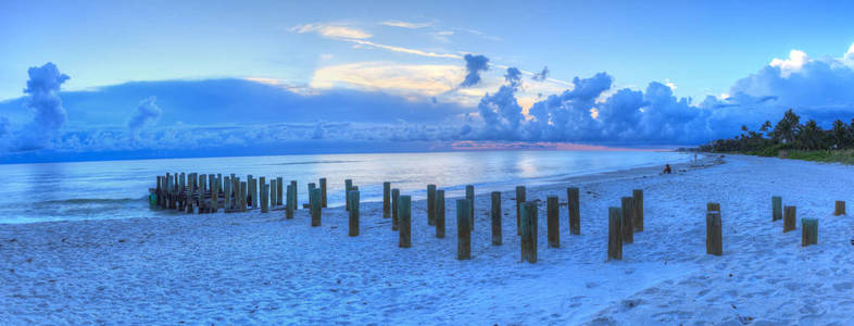 日落上空的老码头在海洋上的那不勒斯海滩与黑暗的天空头顶和雨在地平线上佛罗里达州那不勒斯