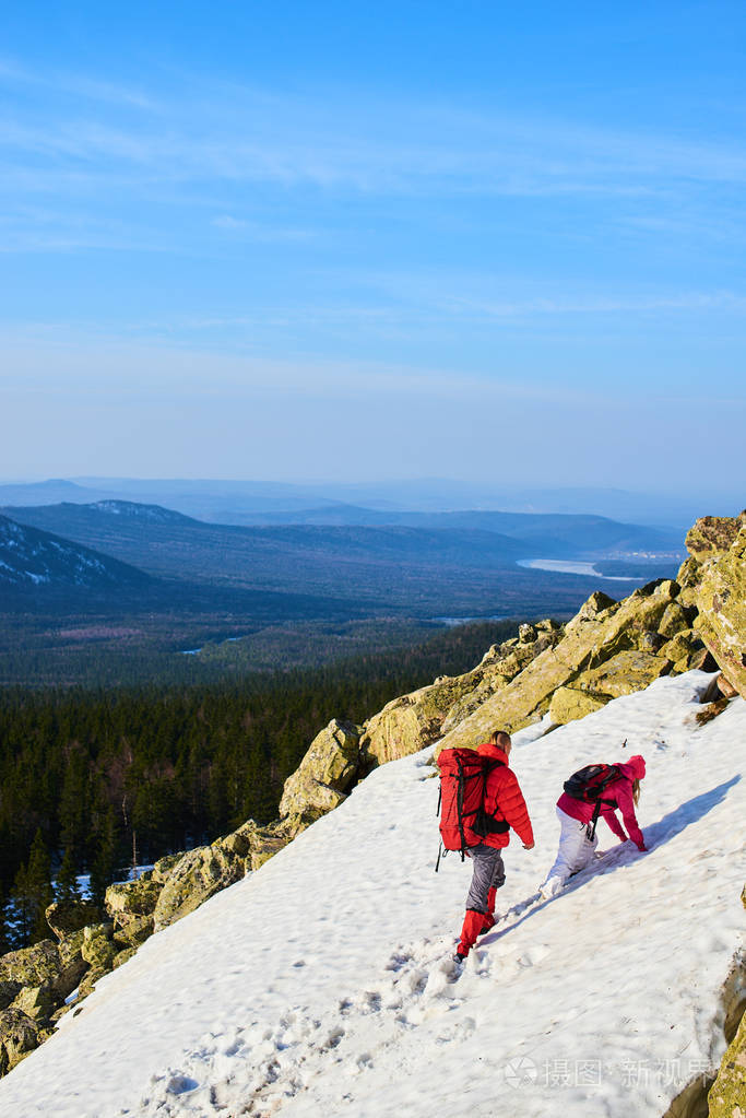 在阳光明媚的日子, 男女背包客爬上雪山
