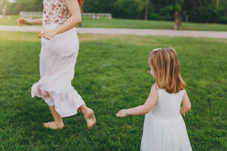 小可爱的婴儿女孩跑追赶与快乐的女人在绿色的草地上的绿草在公园.
