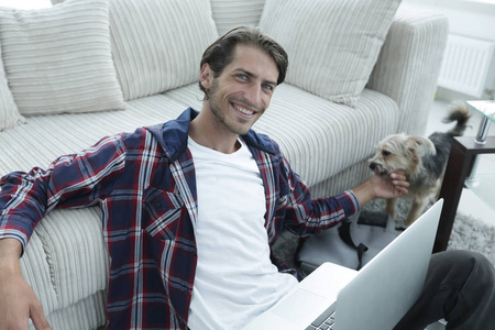 时尚的年轻男人，抚摸着他的宠物和笔记本电脑上工作