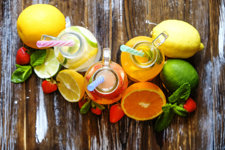 三瓶新鲜冰冷的柠檬水, 不同口味的饮料有柠檬, 橙, 柚子, 石灰, 薄荷叶和草莓 grunged 木桌背景。顶部视图, 复制空