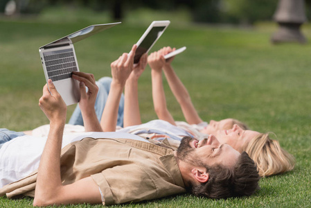快乐的家庭躺在草地上使用数字设备