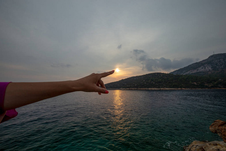 晚上在岩石海岸。在夕阳的背景上的女孩的手上显示