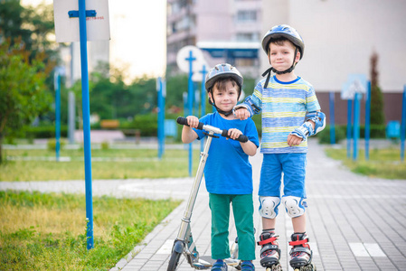两个男孩的轮滑鞋和他的兄弟兄弟骑着摩托车裹在公园里。儿童佩带保护垫为安全轮滑骑马。儿童活动户外运动