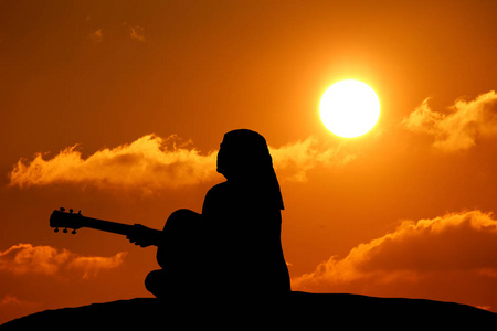 大海磅礴的声音女孩在玩吉他的大海和美丽的日落背景的剪影照片