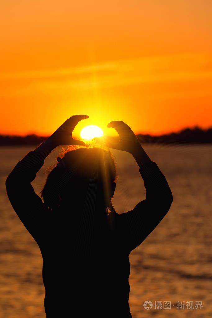 女孩的剪影对黄昏太阳, 红色日落使心脏手对太阳
