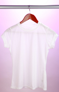 在粉红色的背景上衣架上的白 t 恤照片