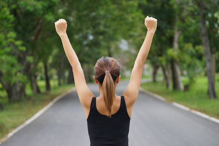 成功的妇女举起胳膊在横穿轨道以后奔跑在夏天日落。健身女运动员与武器庆祝成功和目标后运动锻炼和锻炼