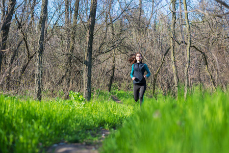 年轻妇女在早晨奔跑通过春天森林