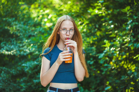 年轻美丽的女孩喝新鲜榨汁的背景下多汁的叶子