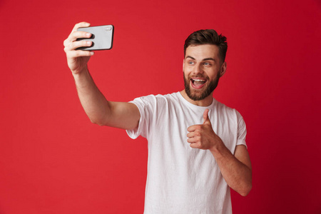 站在红墙背景下的快乐青年形象让自拍用手机竖起大拇指手势