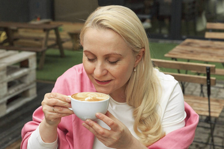 一个穿着粉红色疤痕四十岁的漂亮女人正在咖啡馆里喝咖啡。她看着观众和微笑